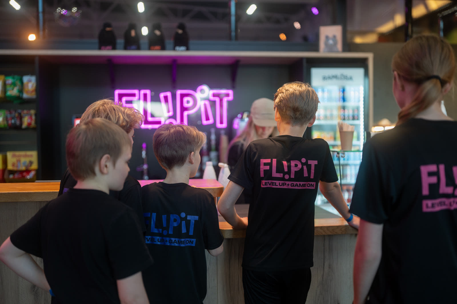Kinder in FlipIt-Shirts an der Theke der Eisbar unter dem FlipIt-Neonschild.