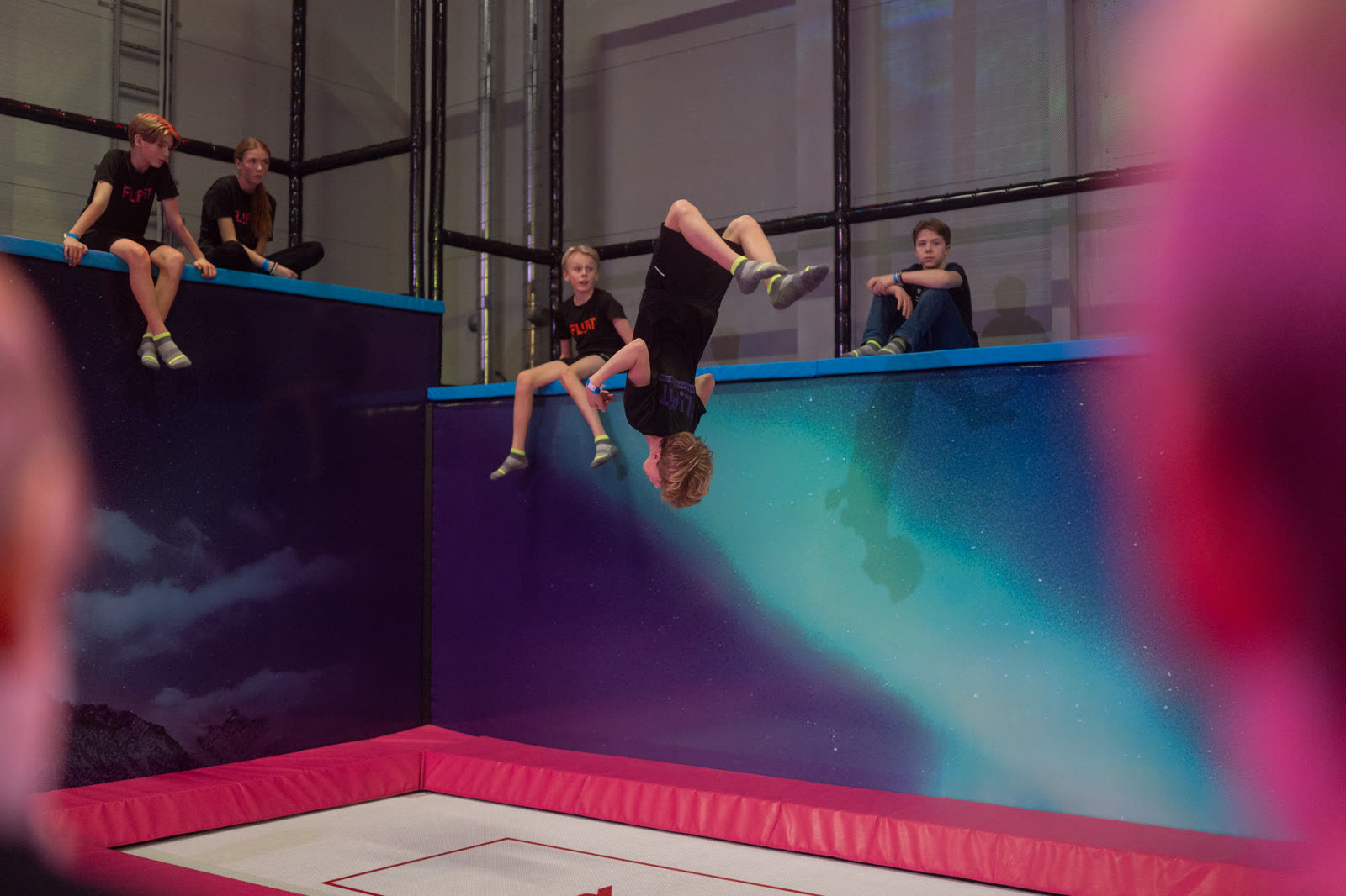 Kompisar vid norrskensväggen på FlipIt, en av dem gör en volt ner mot trampolinen.